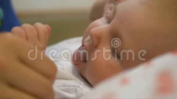 女人嬉戏地抚摸着躺在婴儿床上的一个小孩子的脸颊视频的预览图