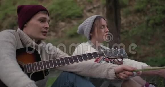 一个带着吉他的朋友和女朋友坐在大自然的篝火前聊天很有趣视频的预览图
