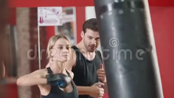 体育女子拳击袋在健身房俱乐部与私人教练视频的预览图