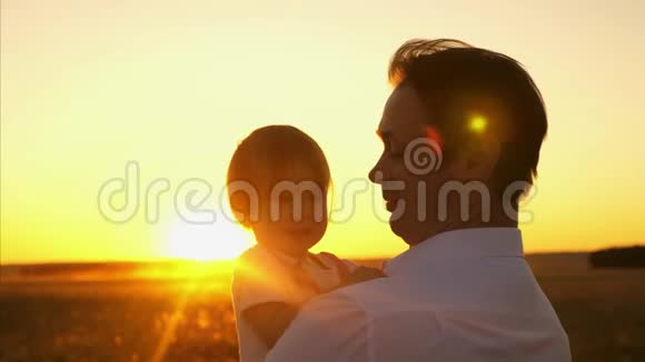 家人爸爸抱着一个小女儿在公园里父亲带着一个小孩子在美丽的夕阳下玩耍视频的预览图