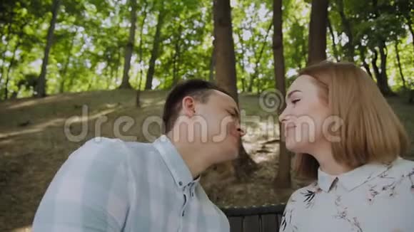 美丽幸福的恋爱情侣坐在公园的长椅上亲吻视频的预览图