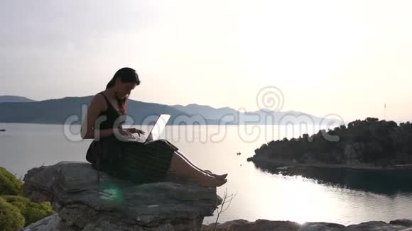 一个漂亮的女学生在海面上的岩石上的笔记本电脑上工作动作缓慢视频的预览图