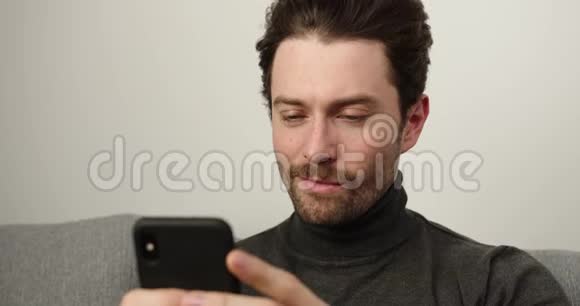 通过互联网观看视频并在家里使用社交网络快乐的黑发男人写短信视频的预览图