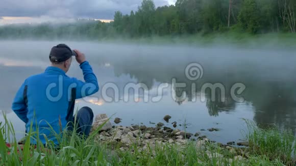 人坐在地上看着平静的河水雾视频的预览图