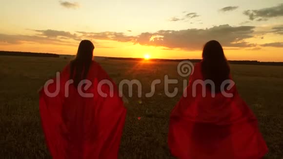 日落时分妈妈和女儿穿着红色斗篷在公园里扮演超级英雄女孩们扮演着穿越田野的超级英雄视频的预览图