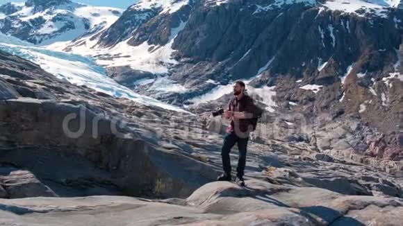 长胡子的旅行者带着背包拍摄挪威冰川的照片视频的预览图