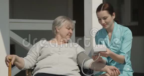 在阳光明媚的日子里护士在养老院拍摄的照片上微笑和照顾老人出门视频的预览图