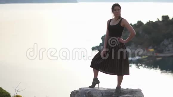 美丽的黑发女人站在岩石上静静地站在大海上慢悠悠地走着视频的预览图