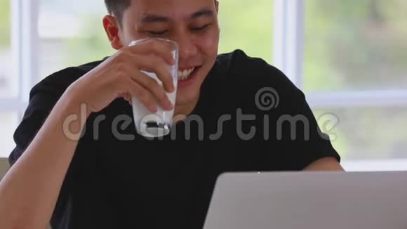男人在客厅喝牛奶和使用笔记本电脑视频的预览图