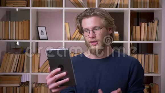 在大学图书馆的平板电脑上播放视频的有魅力的成年男生特写镜头视频的预览图