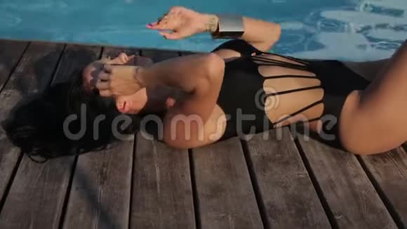 性感的女人黑发穿着优雅的泳衣在露天游泳池附近放松视频的预览图