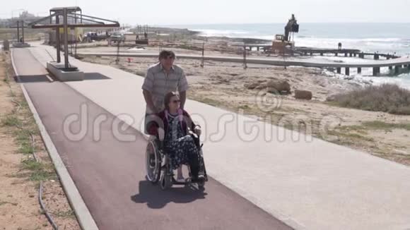 一位老人载着一位坐轮椅的妇女沿着长廊走视频的预览图