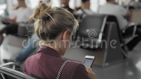 未被识别的年轻女性在坐在机场等待航班时使用智能手机上的社交网络视频的预览图