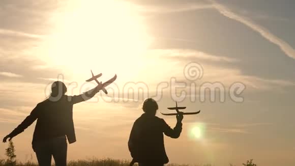孩子们手里拿着一架飞机在太阳的背景下发呆两个女孩在日落时玩玩具飞机剪影视频的预览图