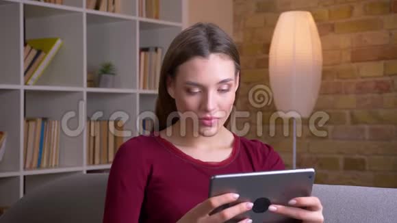 年轻漂亮的黑发女人在家玩平板电脑游戏非常快乐视频的预览图