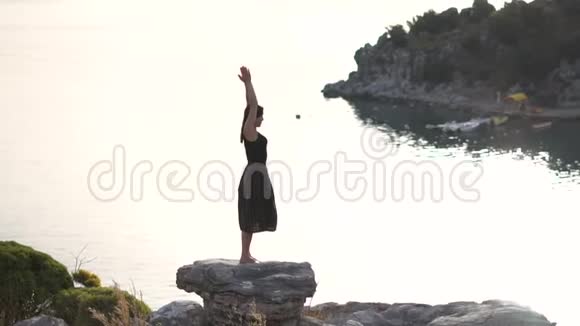 年轻的女孩祈祷并感谢上帝站在海边的岩石上慢动作视频的预览图