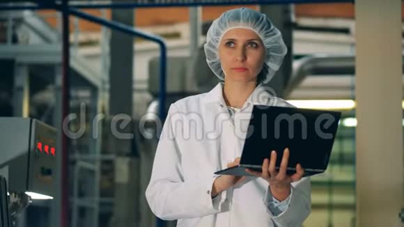 穿制服的漂亮女人正在工厂里操作笔记本电脑视频的预览图