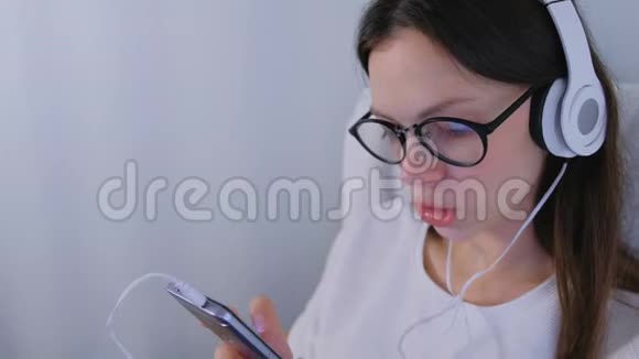 戴眼镜的快乐黑发女人正在智能手机上用耳机听音乐唱一首歌视频的预览图