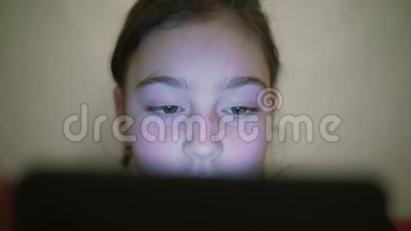 少年女孩夜晚镜头脸上带着淡淡的倒影浏览平板电脑微笑视频的预览图