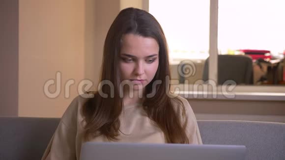 使用笔记本电脑和坐在沙发上看一部滑稽电影的年轻白种人女性的特写镜头视频的预览图