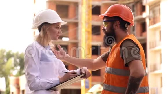 戴防护头盔的建筑工人在施工现场讨论施工现场的施工人员两个工程师视频的预览图