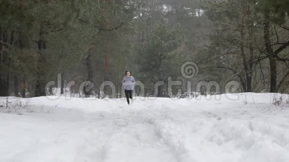 小径跑年轻迷人的白种人女孩在雪地上奔跑在森林里正面静态拍摄视频的预览图
