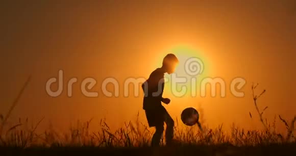 小男孩足球运动员剪影男孩在日落时在球场上插球慢动作视频的预览图