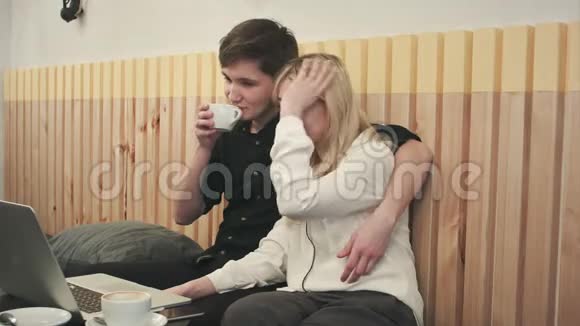 漂亮的年轻夫妇在咖啡馆里带着笔记本电脑他们一起看电影和喝咖啡视频的预览图