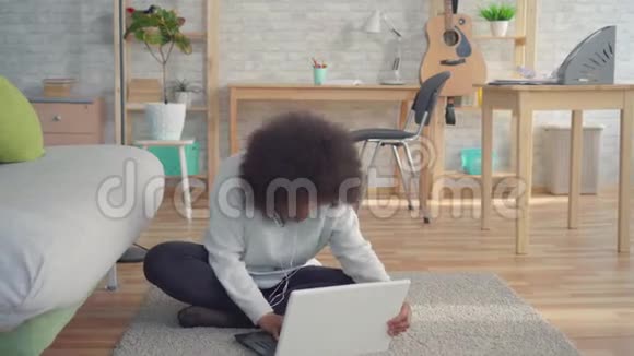 美丽的非洲裔美国妇女她的发型是非洲式的她坐在地上手提电脑了解了这场胜利视频的预览图