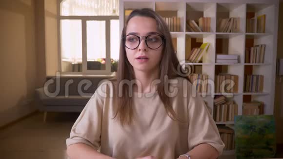 年轻貌美的白种人女性博客作者戴着眼镜在公寓里的室内镜头中交谈视频的预览图