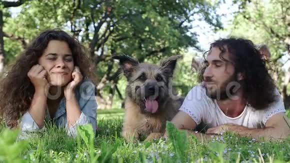 一对年轻快乐的夫妇和他们的狗躺在公园的草地上视频的预览图