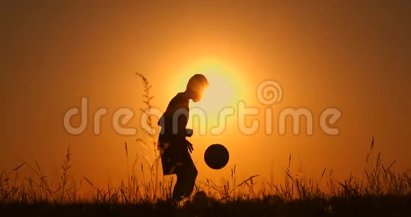 小男孩足球运动员剪影用球练习夕阳红黄金时刻慢动作视频的预览图