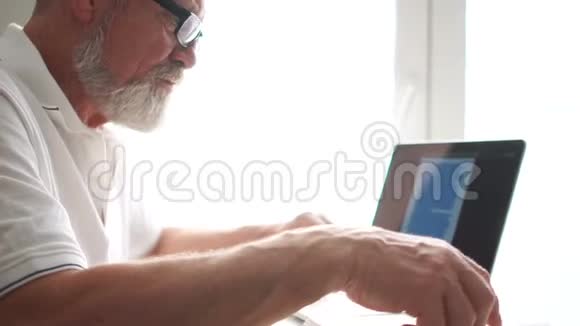 在家用笔记本电脑工作的老人老人在家里用电脑坐在椅子上看屏幕长者视频的预览图