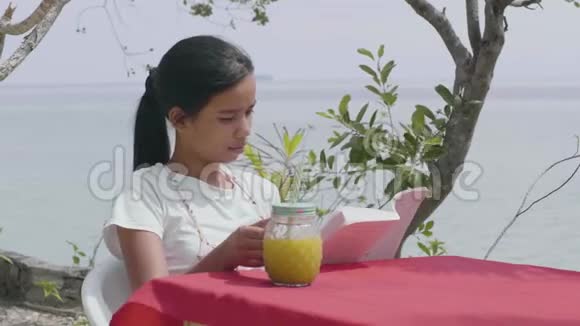 夏天漂亮的女人在海边的桌子上看书喝果汁视频的预览图