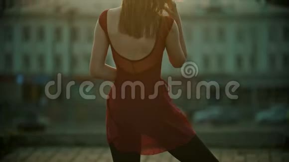 一位年轻优雅的红衣女子站在屋顶上修头发日落视频的预览图