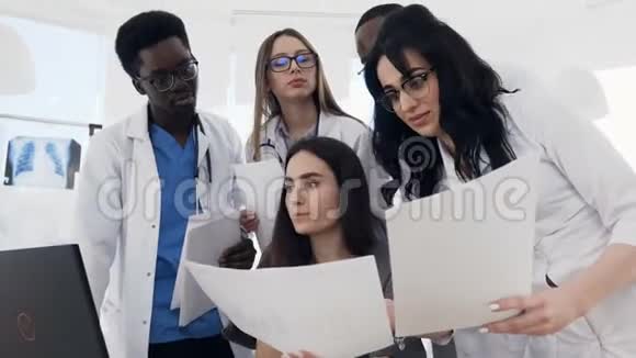 年轻的跨国医生在医院开会工作日使用笔记本电脑和纸质文件视频的预览图