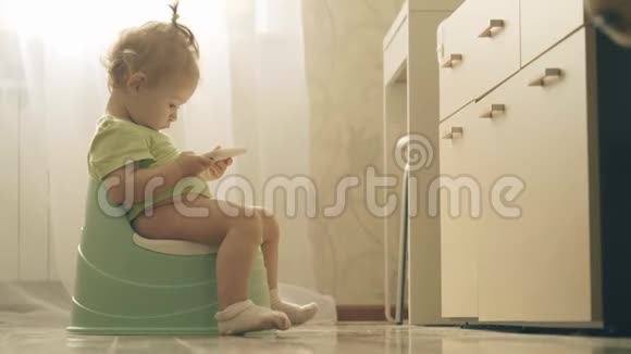 小女孩坐在马桶上看着智能手机上的卡通片视频的预览图