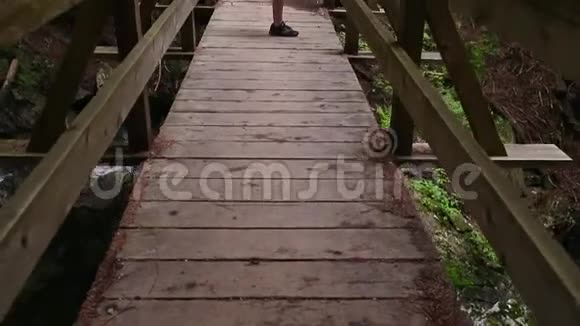 一个年轻女子穿着运动用品在一座常绿森林里的木桥上伸展着一条小溪的全景视频的预览图