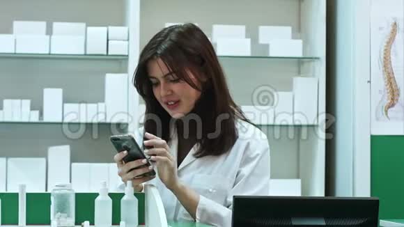 年轻的女药剂师用手机发短信微笑着和她的男同事交谈视频的预览图