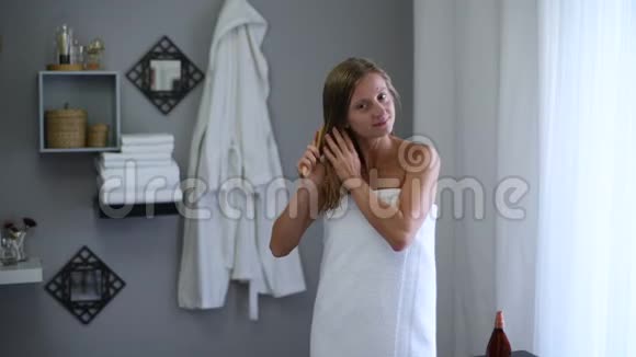 洗完澡后裹着毛巾的漂亮女人擦了擦湿头发涂上椰子油视频的预览图