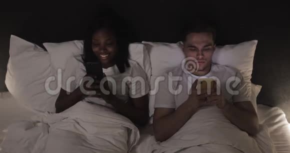 快乐的多民族夫妇床上有智能手机人技术互联网和传播理念视频的预览图