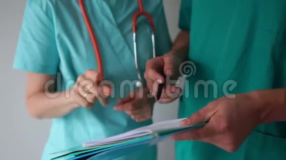 男人和女人穿着医用长袍用听诊器文件夹和笔说话密切医生手中讨论病人视频的预览图