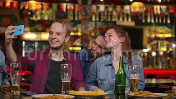 朋友们正在酒吧里用智能手机自拍年轻人摆姿势笑着说话啤酒瓶和视频的预览图