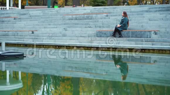 伤心的女孩坐在楼梯上在公园湖里沉思视频的预览图