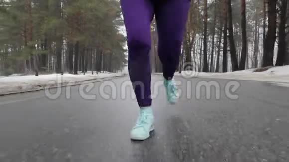 年长的白种人女孩戴着耳机在冬天的雪地公园里跑步双腿收拢前方跟进射击视频的预览图