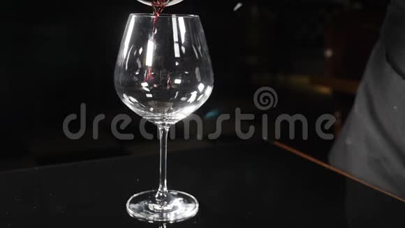 红酒在黑色背景下倒入酒杯中慢动作将红酒从瓶颈倒入玻璃杯中关闭视频的预览图