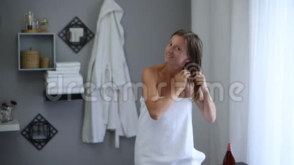 淋浴后裹着毛巾的漂亮女人用椰子油抹她湿漉漉的头发视频的预览图