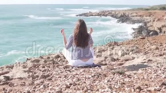 一个年轻的女人正坐在海边悬崖上的莲花座上视频的预览图