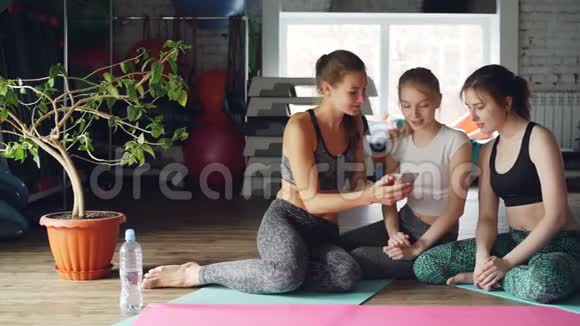年轻女性正在健身房社交看智能手机他们触摸屏幕打手势有感情地聊天视频的预览图