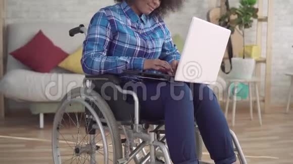 残疾的非裔美国妇女一个坐在轮椅上有非洲发型她用笔记本电脑看相机视频的预览图